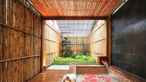 A traditional Japanese onsen with wooden flooring, a hot spring, and a bamboo fence.