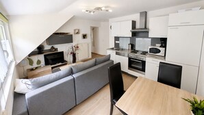 A modern kitchen with a dining area, a grey sofa, and a wooden dining table. - Wald Villa Üssbach (Alf)