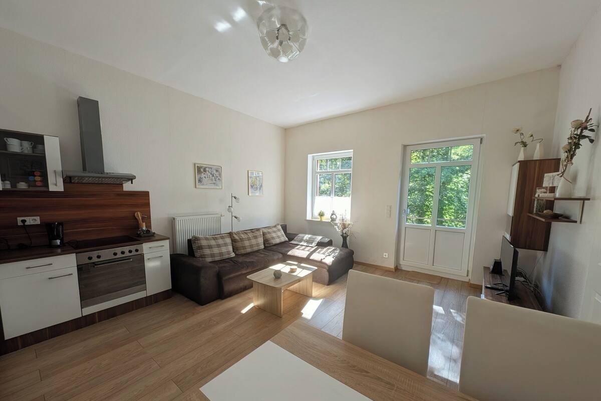 A spacious living area with a sofa, coffee table, and a kitchen area with a stove and cabinets.