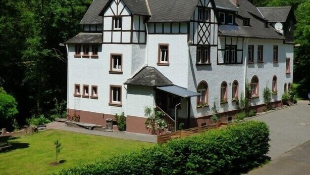 A large, two-story building with a steeply pitched roof, multiple windows, and a small porch area. - Wald Villa Üssbach (Alf)