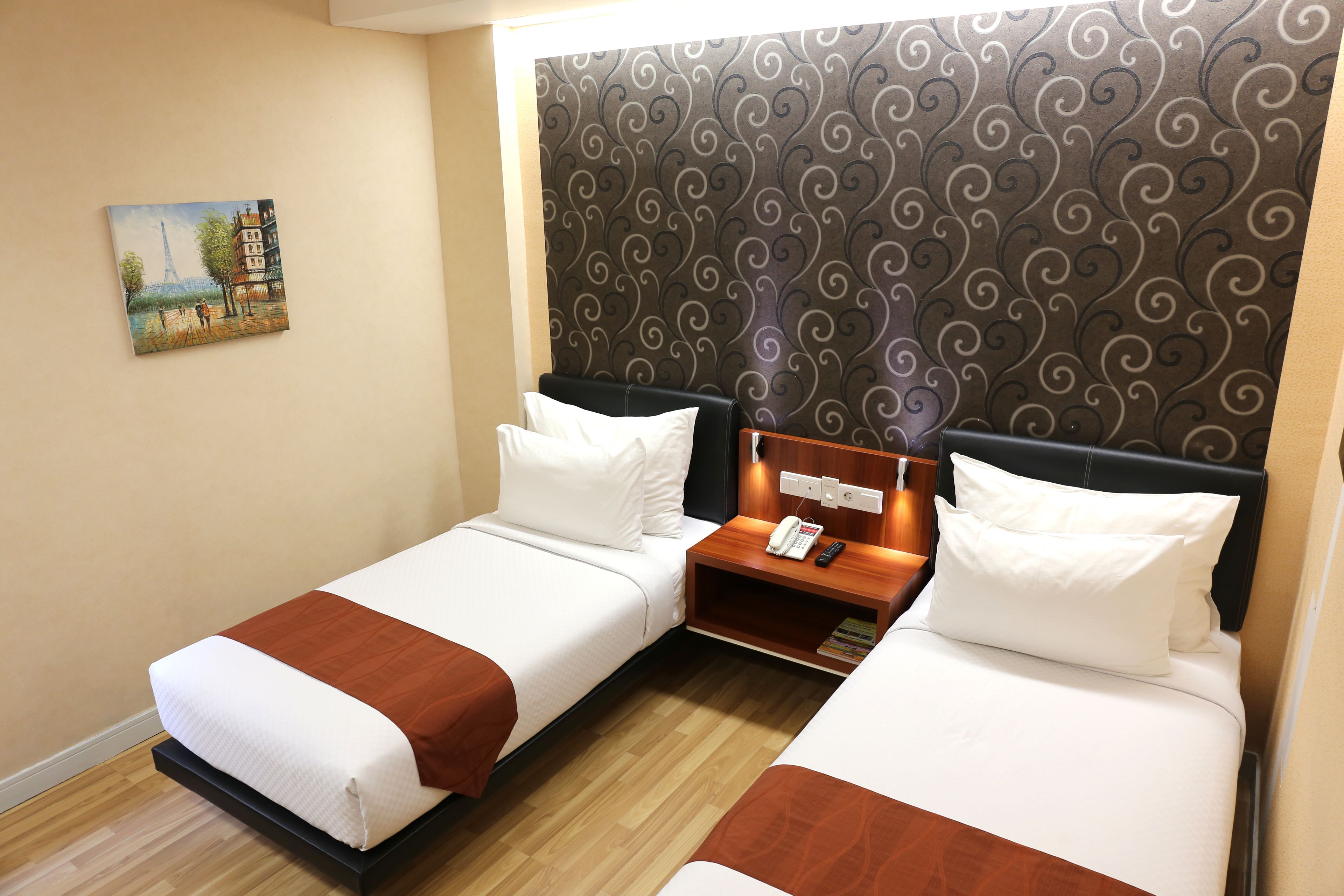 Quarto de hotel com duas camas, uma mesa de cabeceira de madeira com telefone e uma pintura da Torre Eiffel.