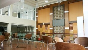 A spacious indoor area with modern furniture, a large flat-screen TV mounted on a wall, and a high ceiling with hanging lights. - Citihub Hotel @Gejayan, Yogyakarta (Yogyakarta)