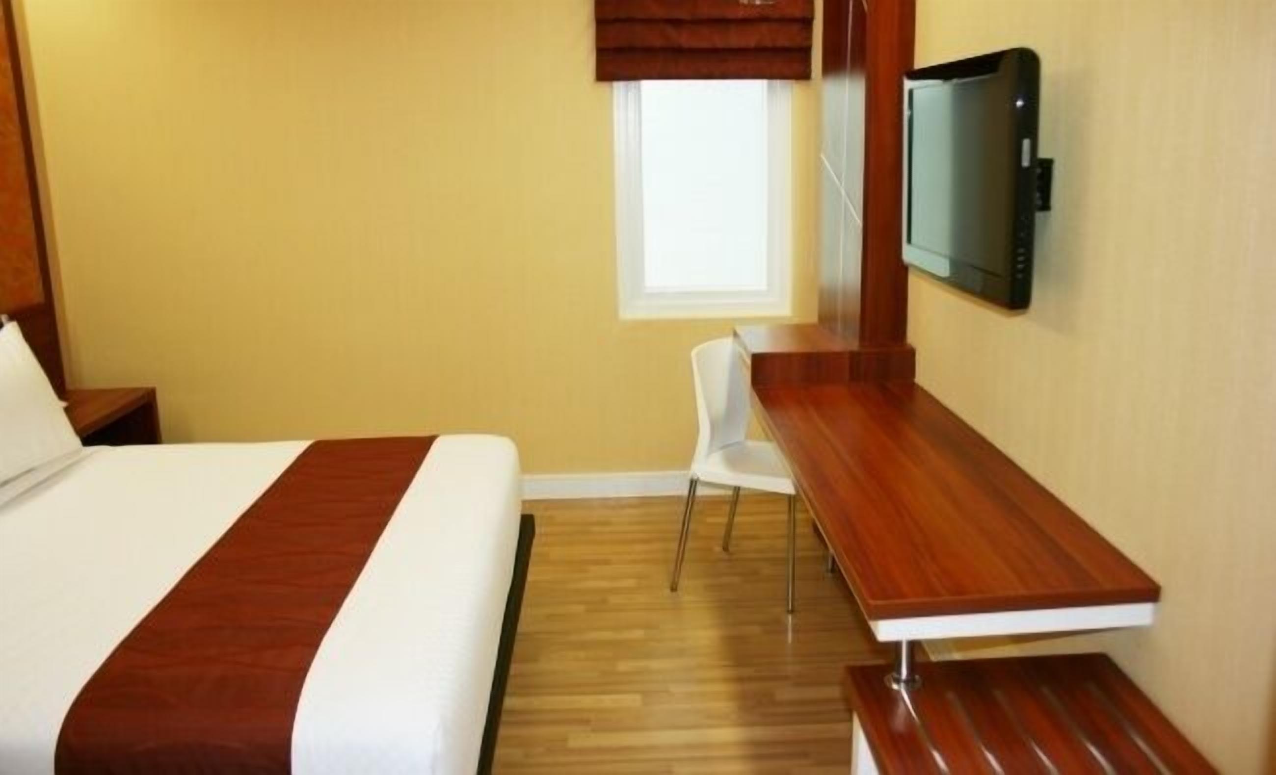 A hotel room with a bed, a desk, a chair, and a TV mounted on the wall.