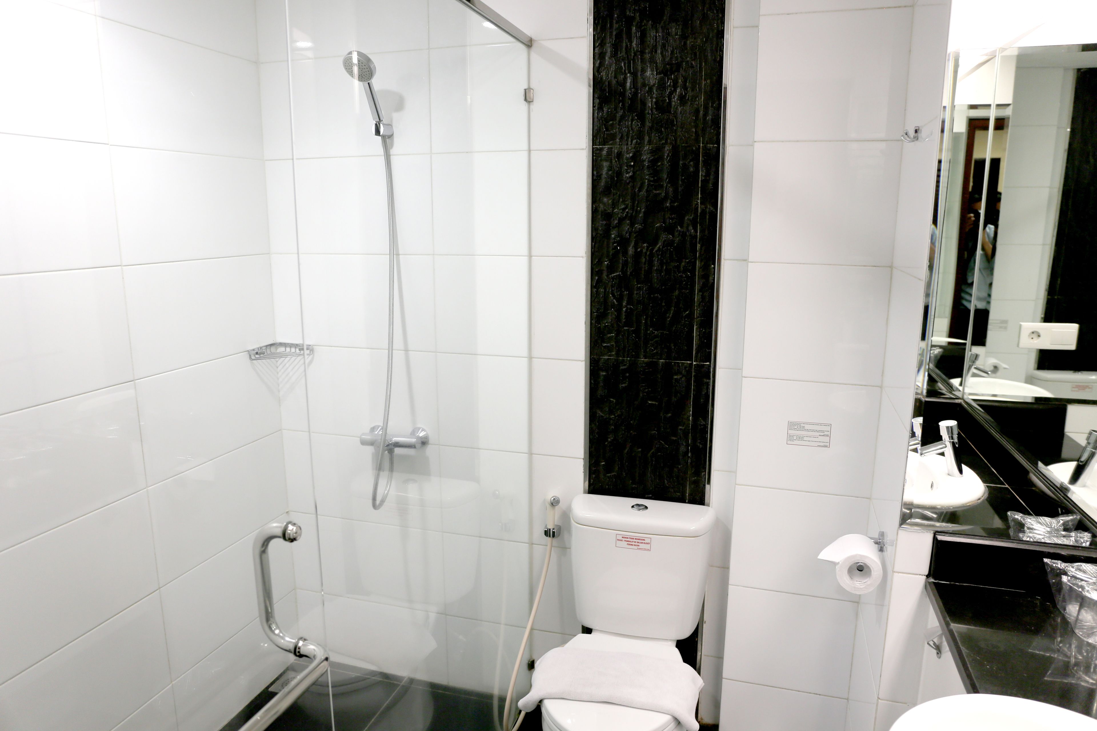 A modern bathroom with white tiles, a glass shower enclosure, a toilet, and a sink with a black countertop.
