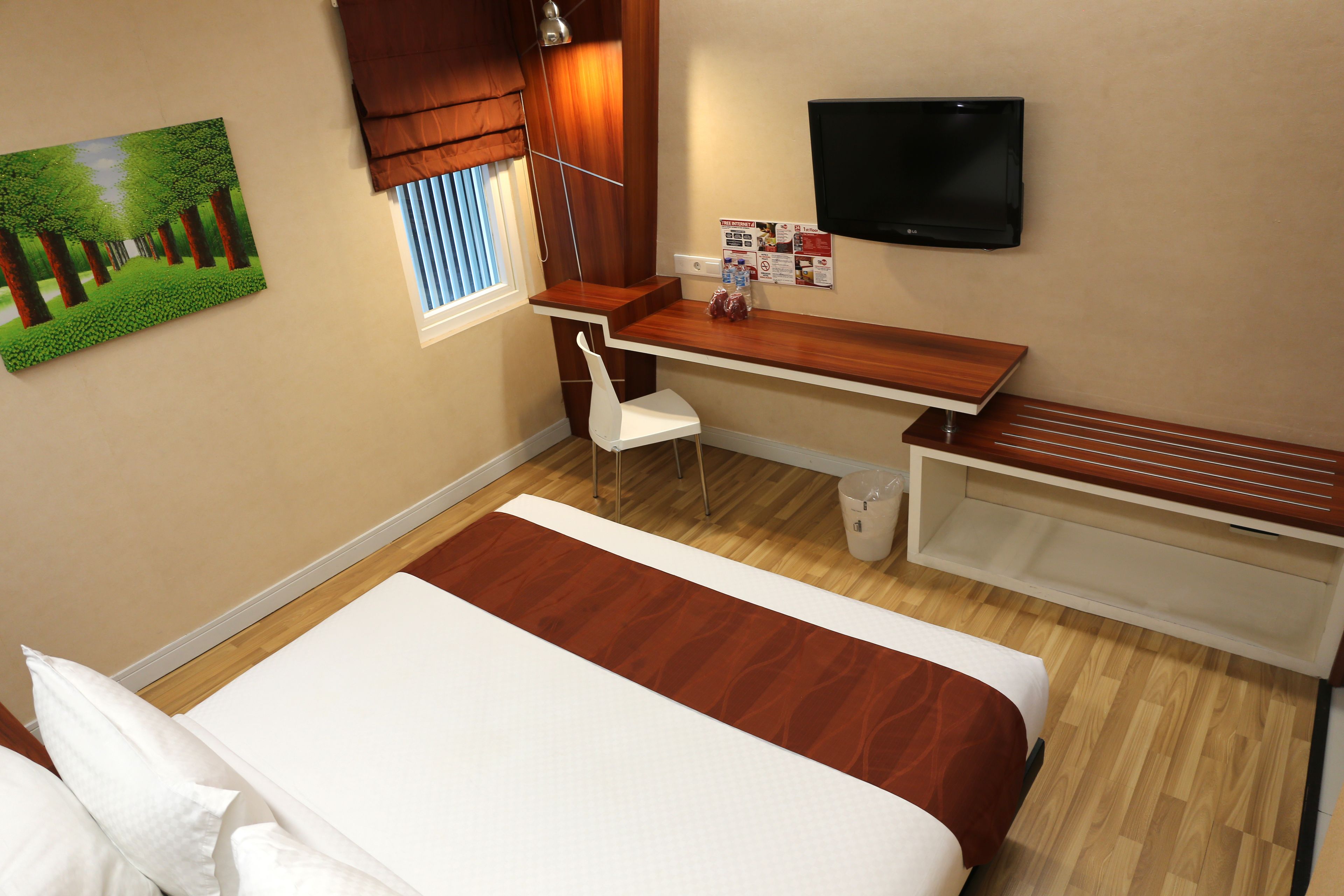 A hotel room with a bed, a desk, a chair, a TV, and a window with blinds.