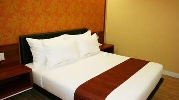 A neatly made bed with white linens and a brown accent, a wooden headboard, and a wooden nightstand with a lamp.