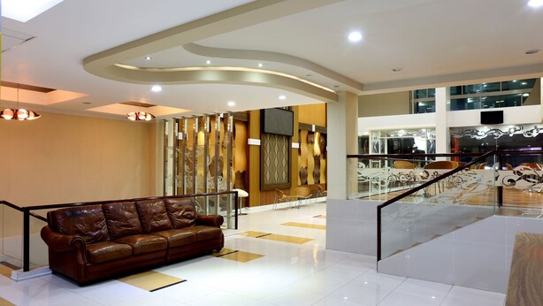A modern lobby with a leather sofa, a staircase, and a decorative wall. - Citihub Hotel @Gejayan, Yogyakarta (Yogyakarta)