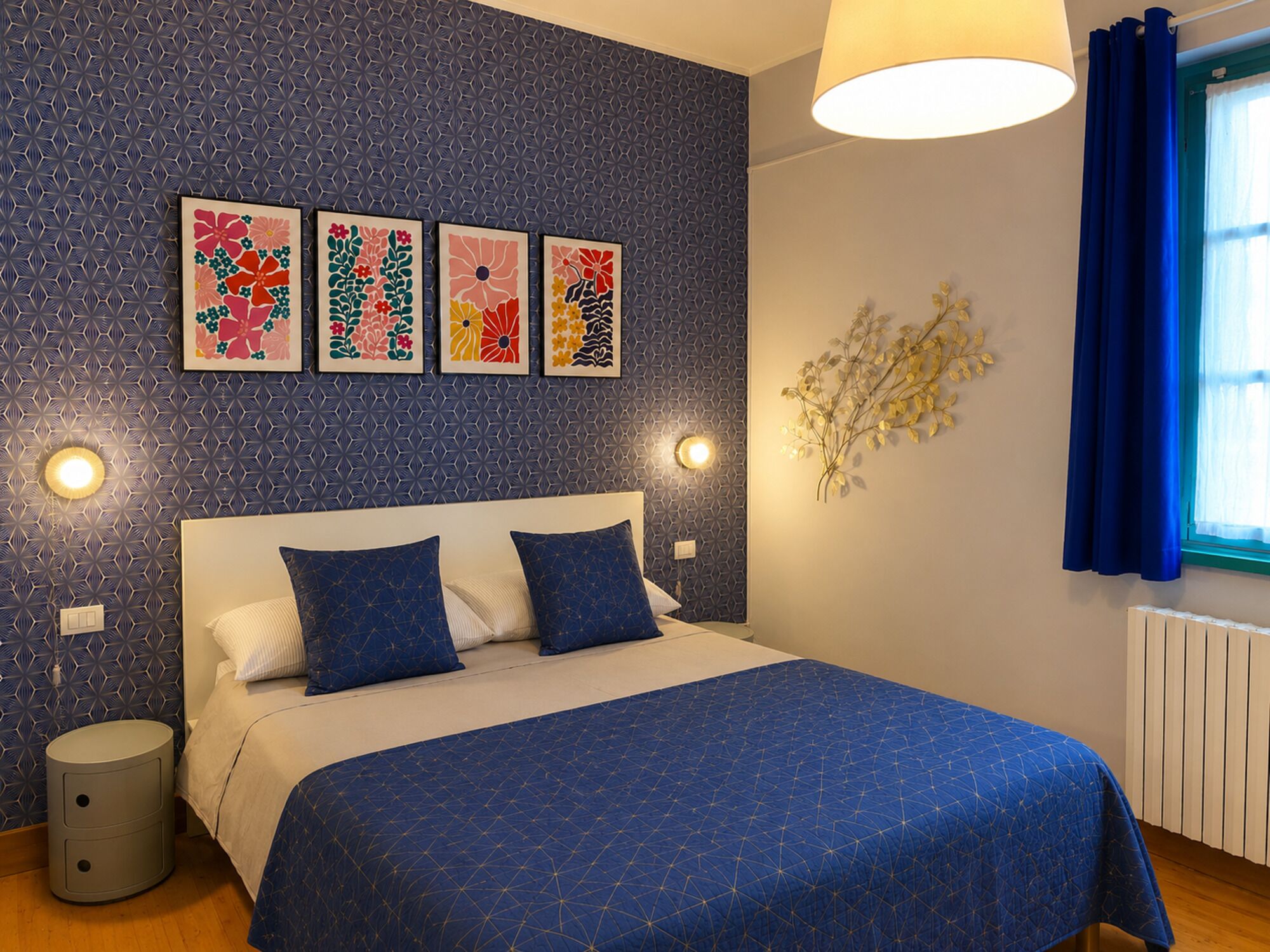 Una camera da letto con un letto, opere d'arte a parete, un comodino e una finestra con tende.