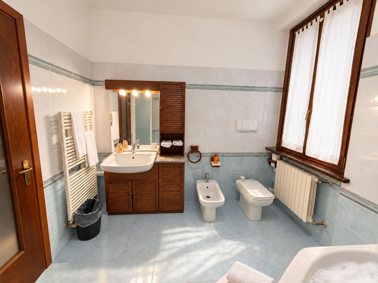 Une salle de bain avec deux vasques, un bidet, des toilettes, une baignoire et un miroir avec éclairage.