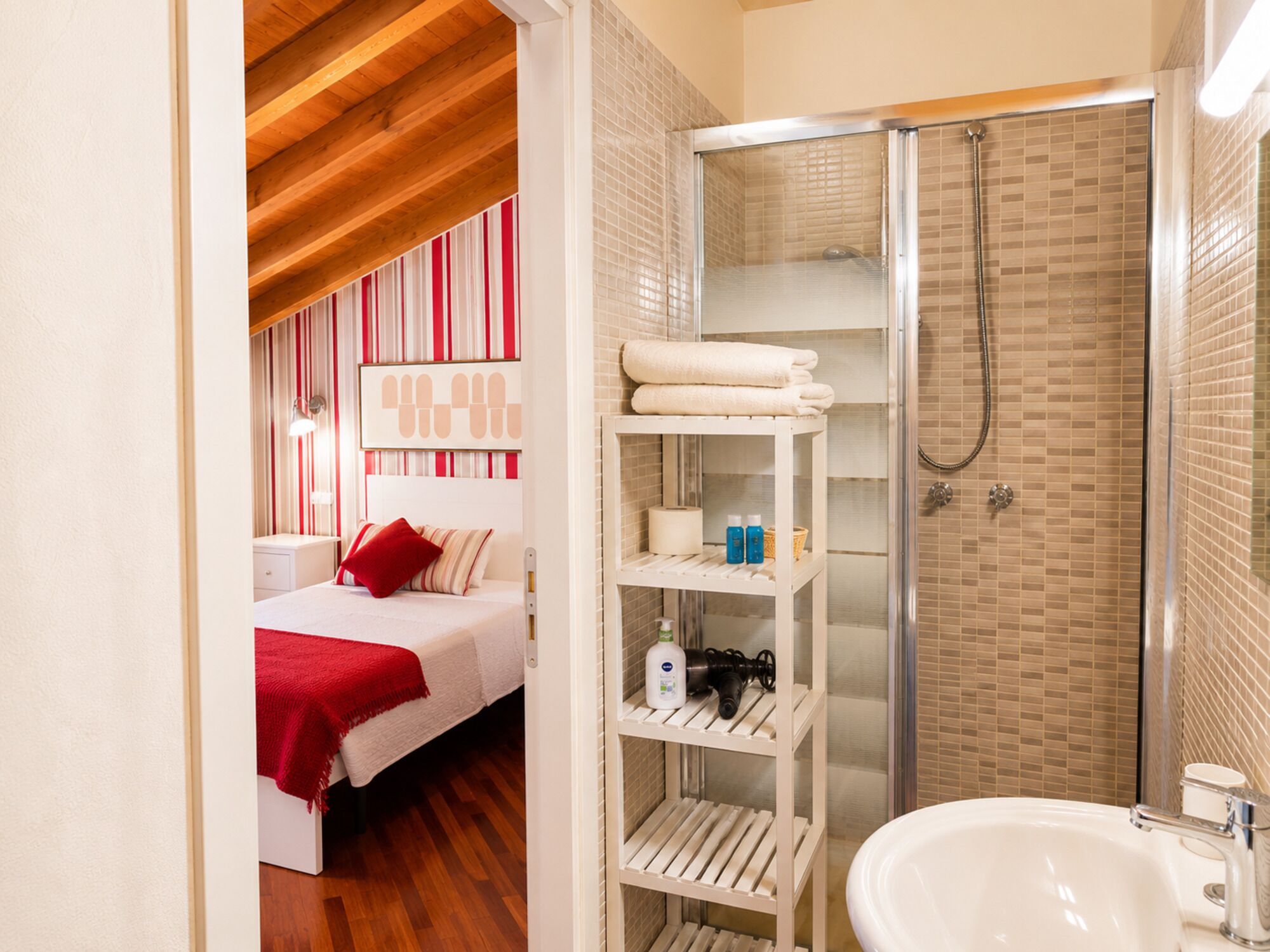 Una camera d'albergo con un letto, uno scaffale bianco con articoli da toilette, una doccia e un lavandino.