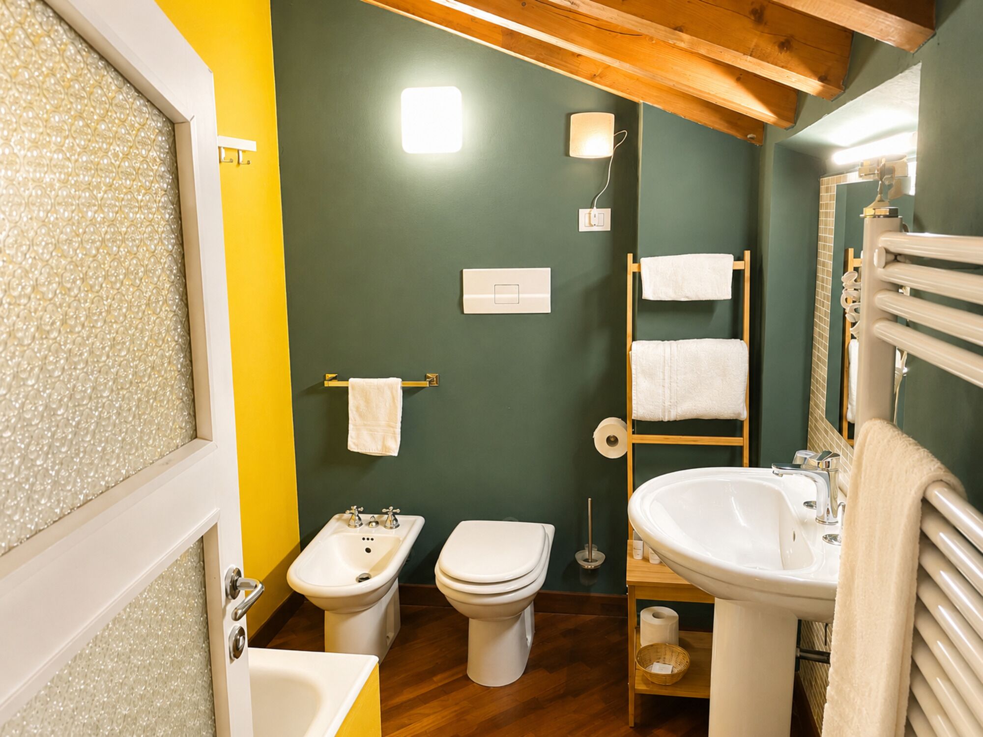 A bathroom with a bidet, toilet, sink, and towel rack.