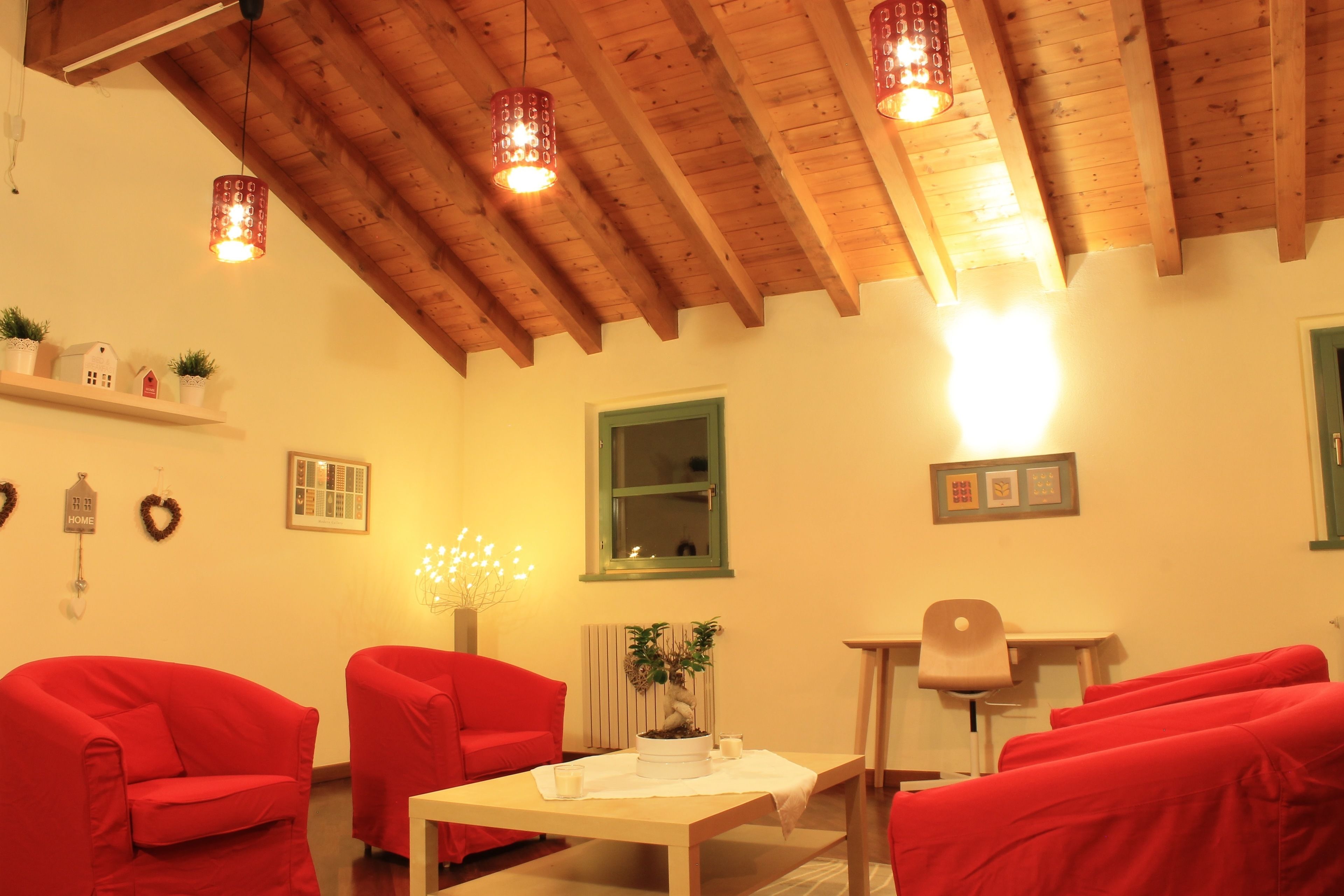 Una stanza accogliente con travi in legno, sedie rosse, un tavolo con una pianta e lampade a sospensione.