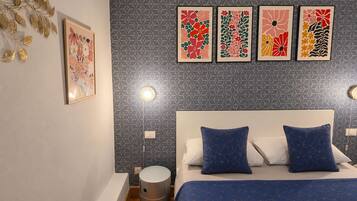 Un dormitorio con cama, almohadas, una lámpara en la pared y un cubo de basura.