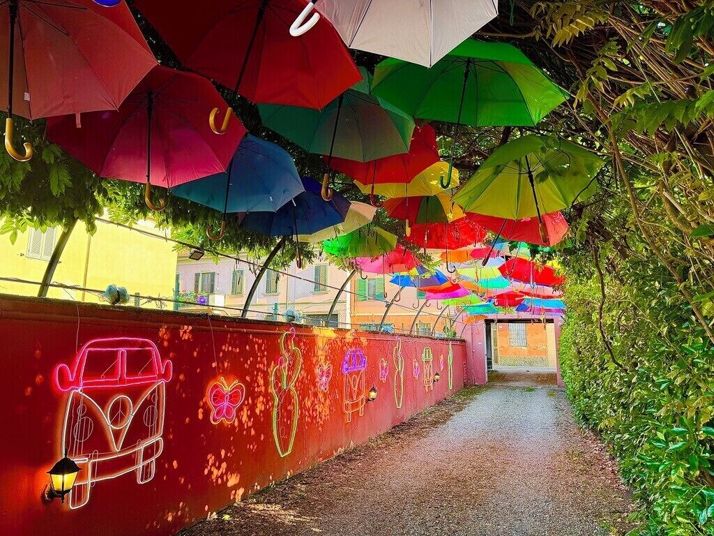 Un camí flanquejat per ombrelles de colors i un dibuix de cotxe de neó a la paret.