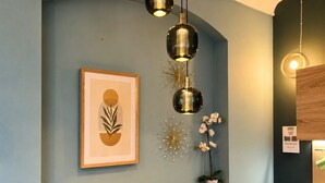 Una pared con un cuadro enmarcado, una lámpara colgante y una pequeña estantería con una planta en maceta.