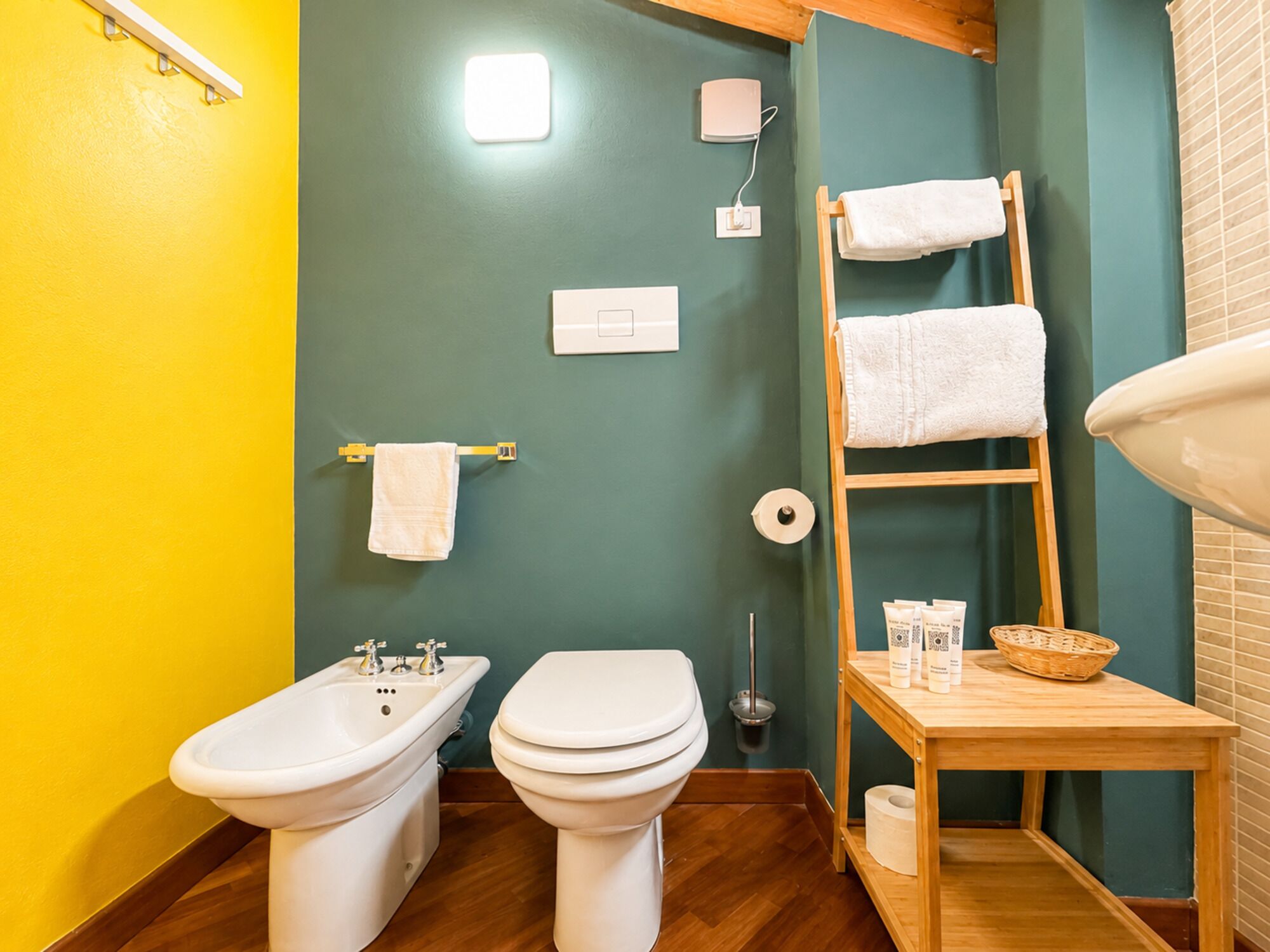 Ein Badezimmer mit integriertem Bidet, Toilette, Handtuchhalter und einem Holzboden mit Pflegeprodukten.
