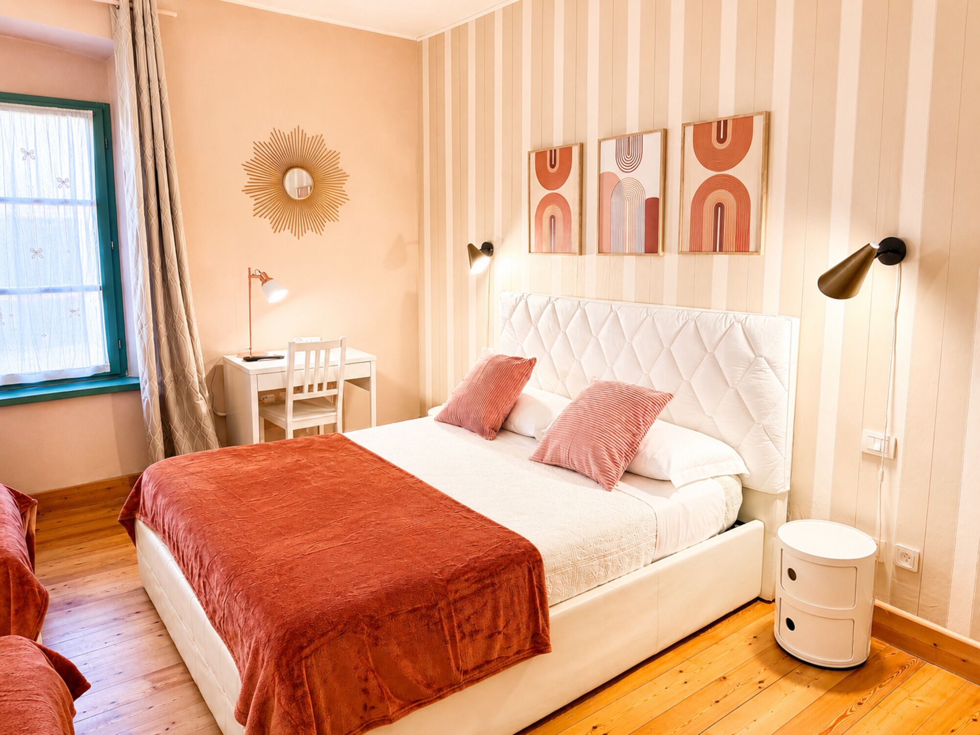 Un dormitorio con cama, mesita de noche, lámpara y un cubo de basura blanco pequeño.