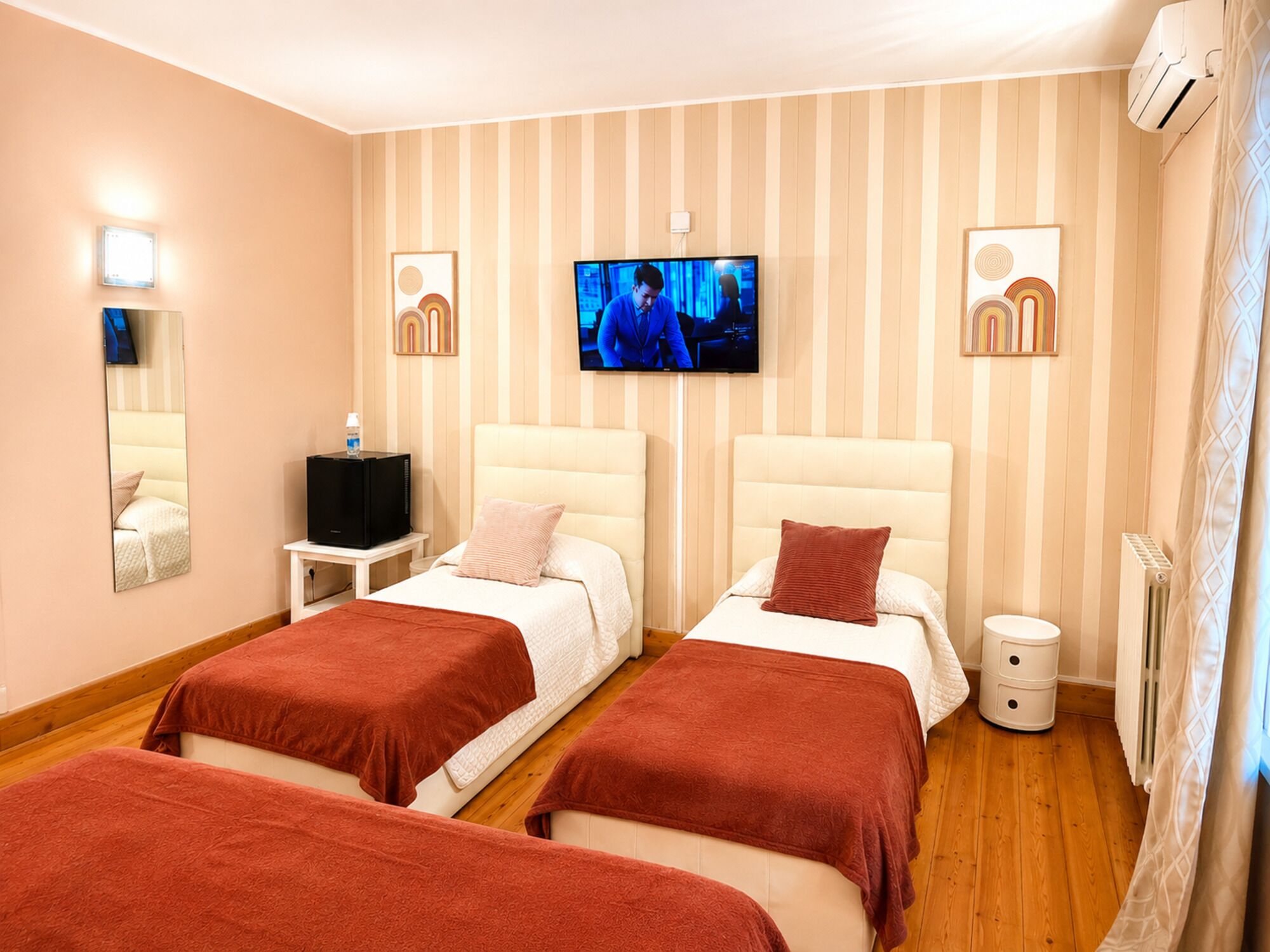 Una camera d'albergo con due letti, una televisione, un tavolino con un mobile porta TV e un termosifone.