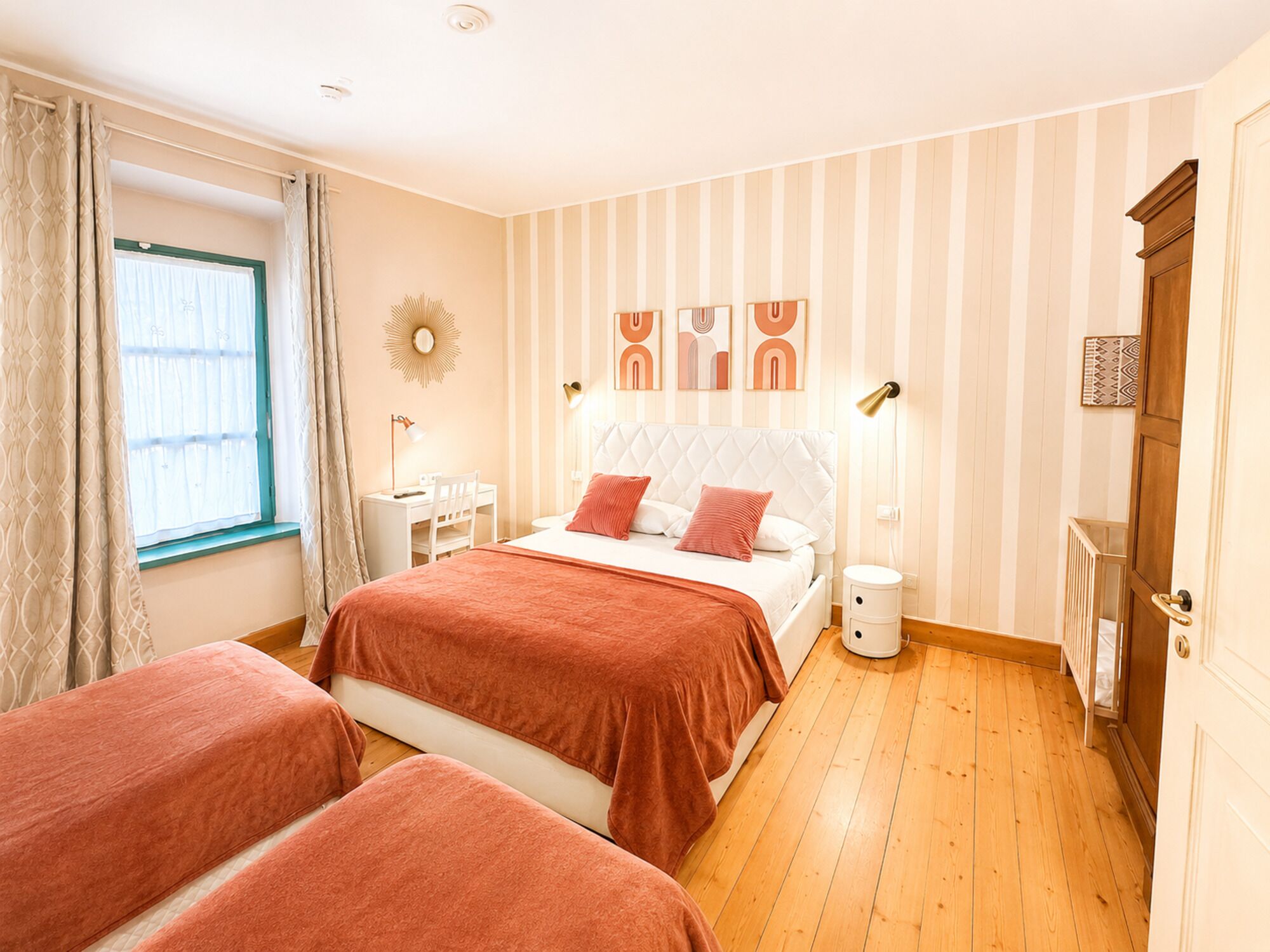 Une chambre à coucher comprenant un lit, deux tables de chevet, un bureau, une chaise et une fenêtre avec des rideaux.