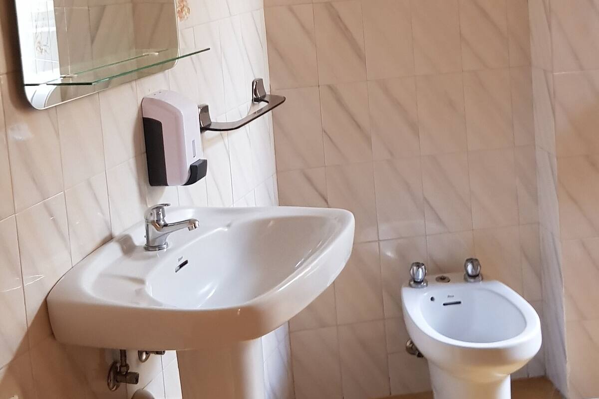 Een badkamer met een witte wastafel, een bidet, een glazen plankje met een zeepdispenser en een spiegel.