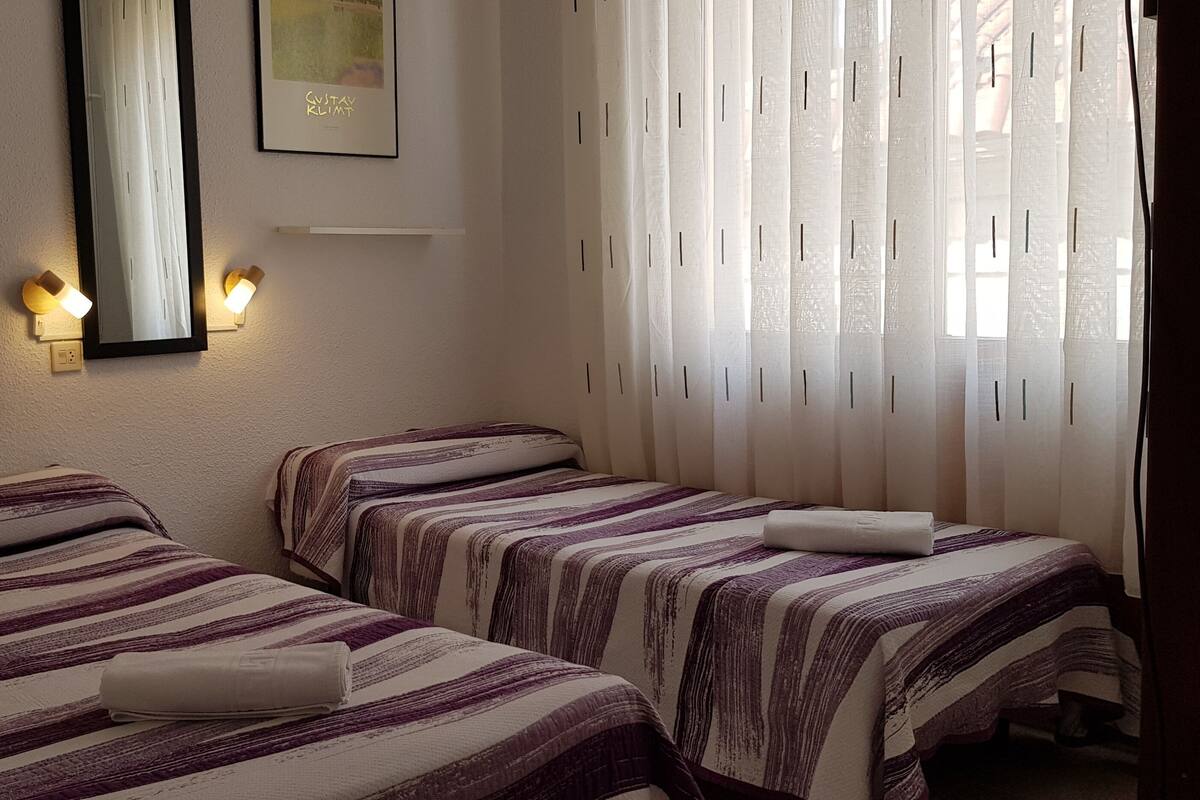 Een hotelkamer met twee bedden, elk voorzien van gestreept beddengoed en een opgevouwen handdoek op het bed. Er zijn wandlampen en een ingelijste foto boven de bedden.