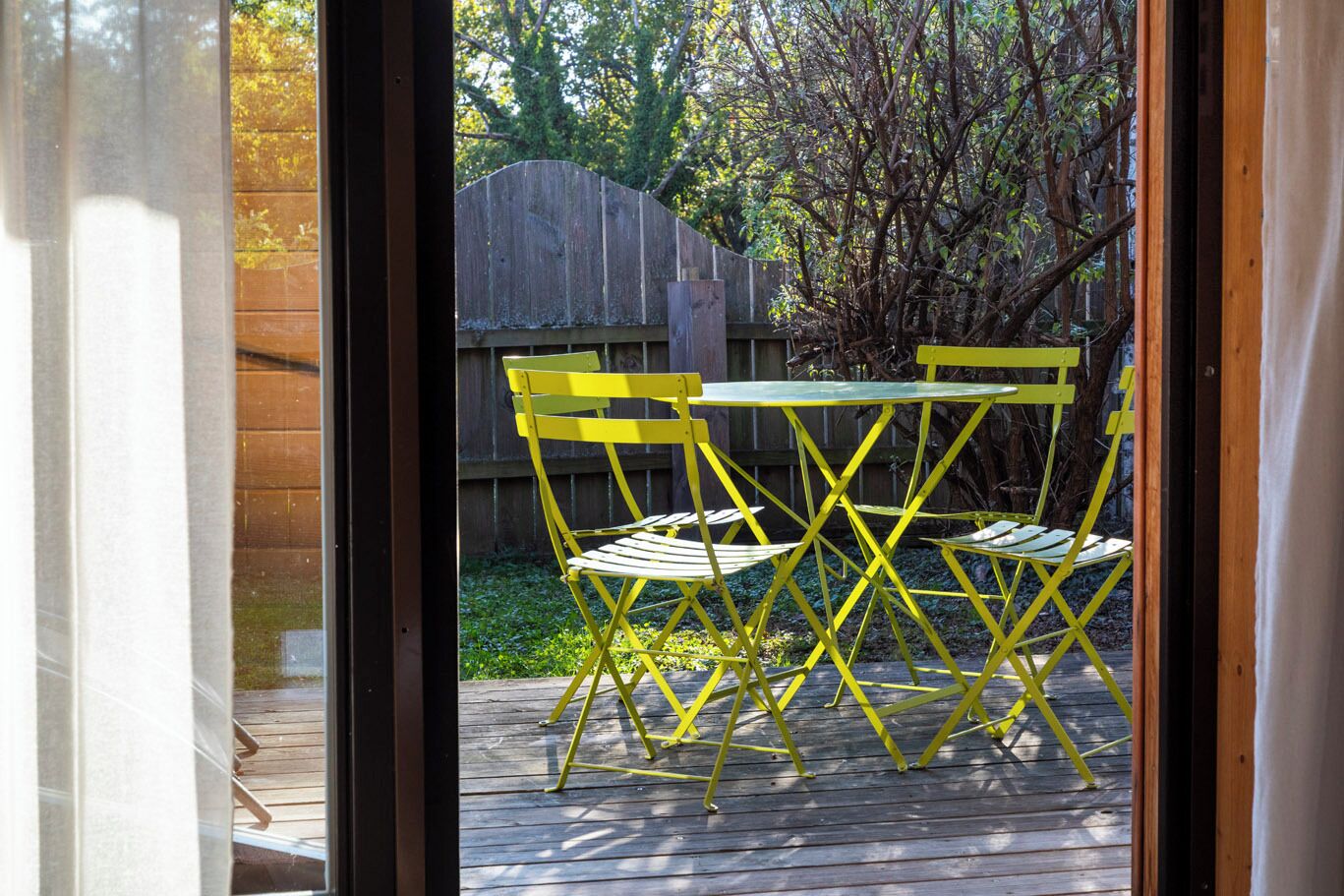 A wooden deck with yellow chairs and a table, viewed through a doorway.