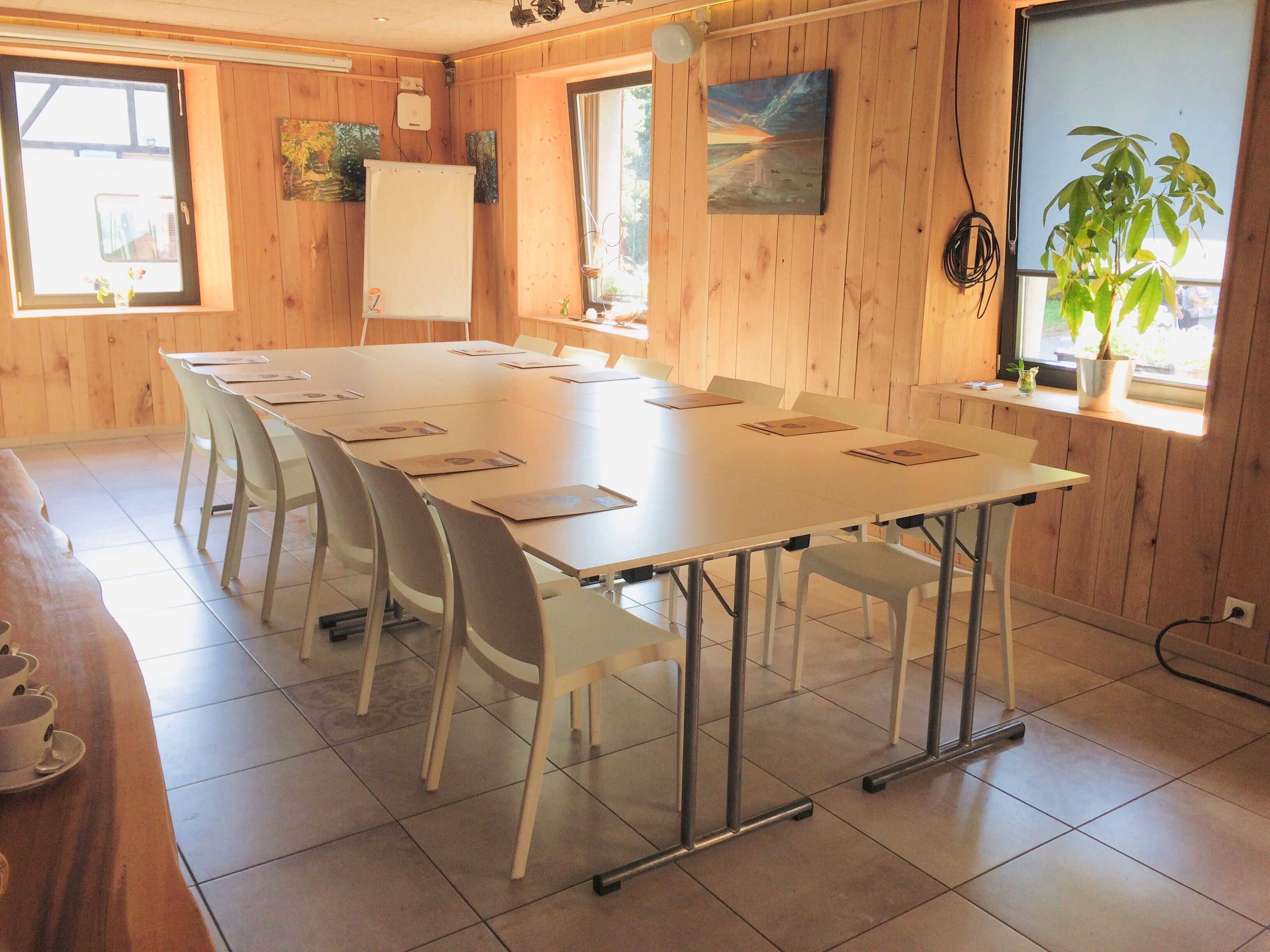Une salle de conférence avec une longue table, des chaises, un tableau blanc et un tableau accroché au mur.