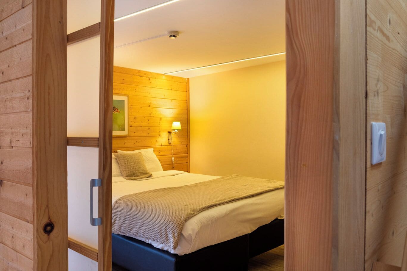 A wooden-paneled room with a bed, a wall-mounted lamp, and a ceiling light.