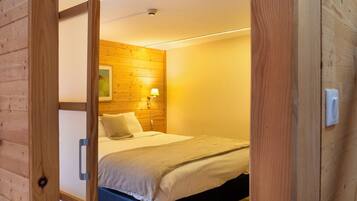 A wooden-paneled room with a bed, a wall-mounted lamp, and a ceiling light.