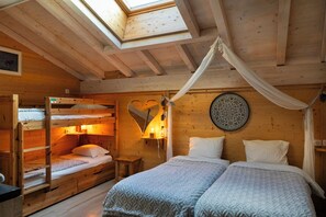 A cozy wooden cabin bedroom with bunk beds, a canopy bed, a heart-shaped wall decoration, and a circular wall hanging.