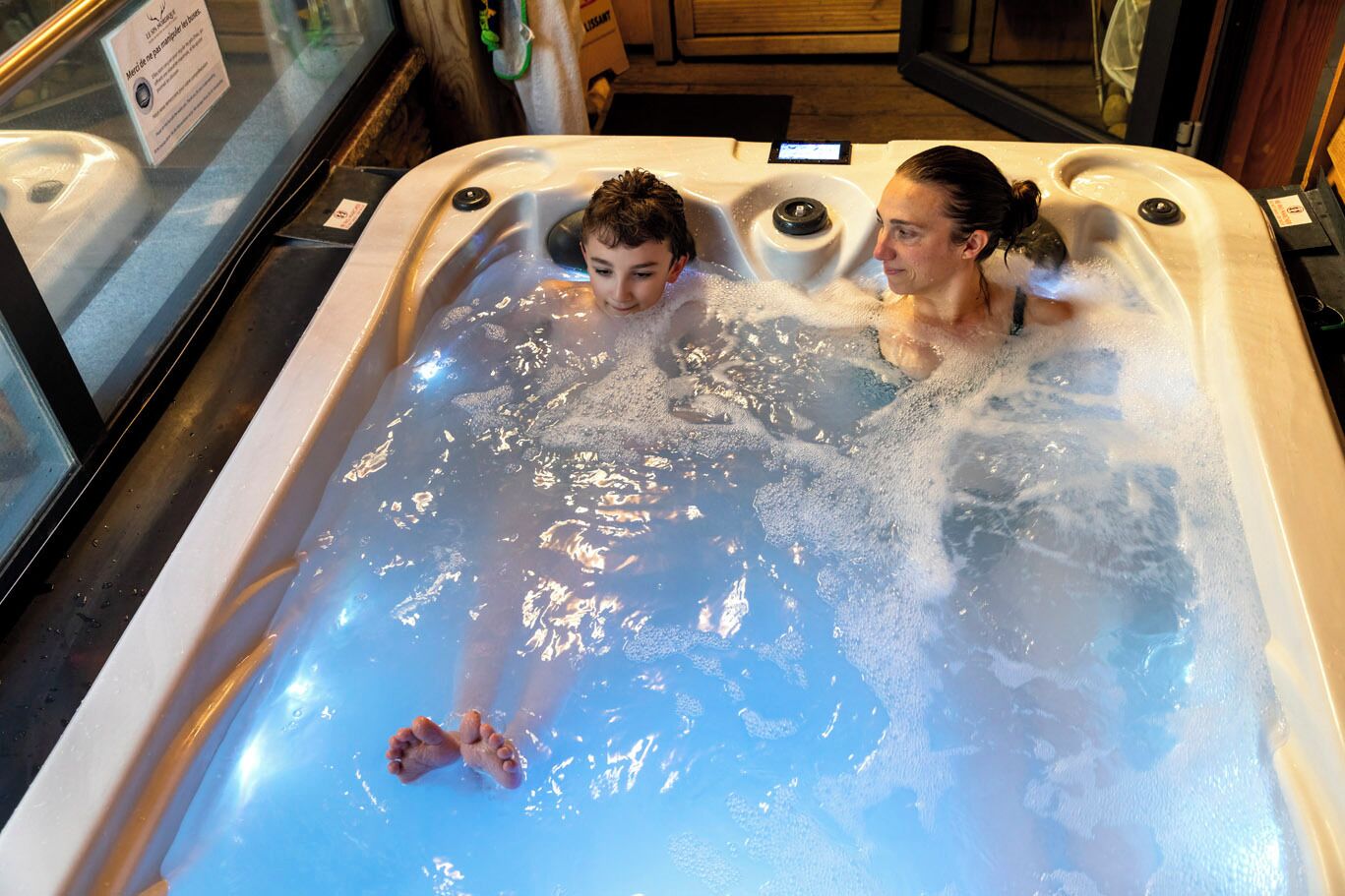 A hot tub with two people in it, surrounded by a glass enclosure.