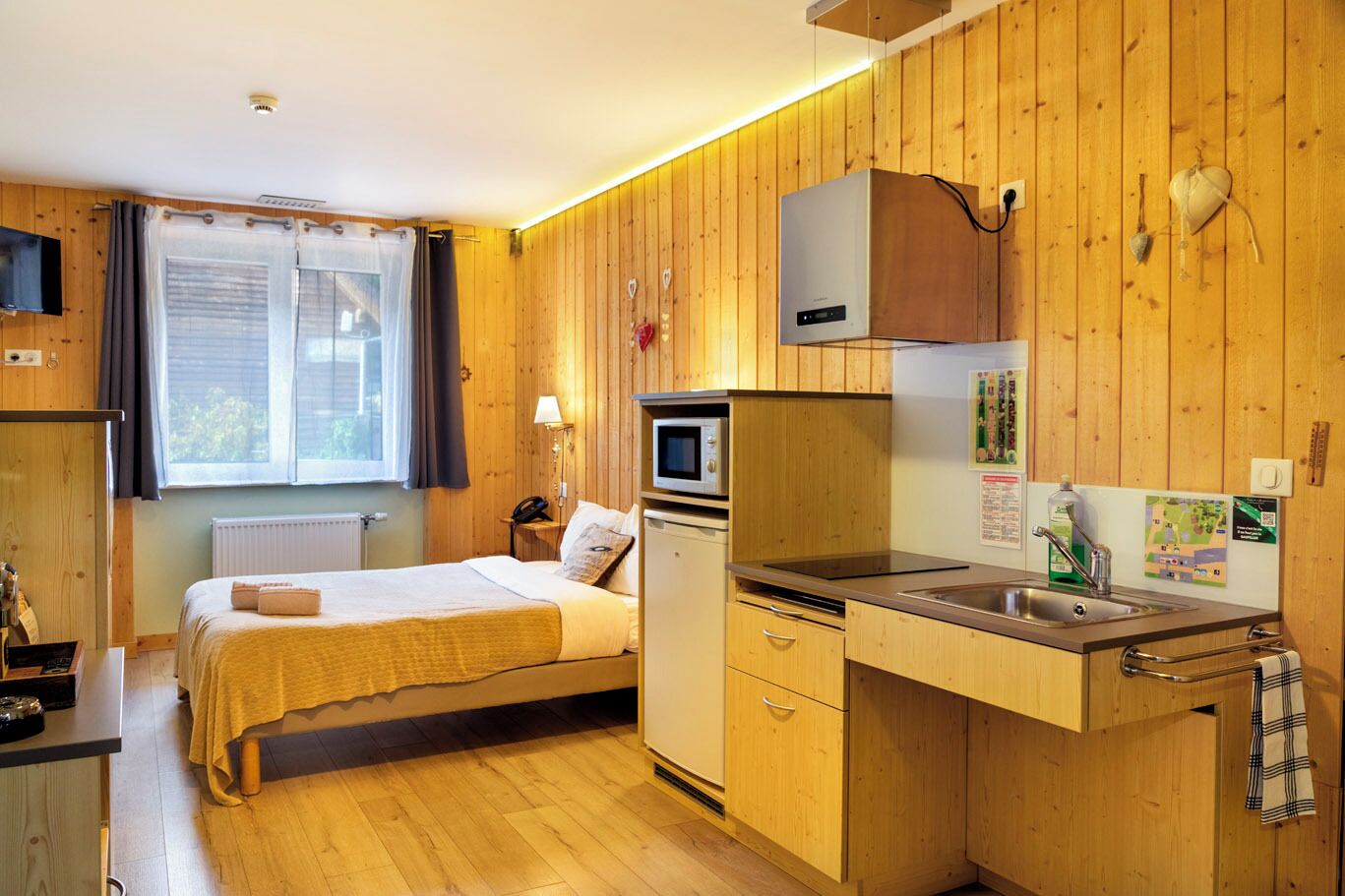 Ein kompakter Raum mit einem Bett, einer Küchenzeile und einem Vorhangfenster.