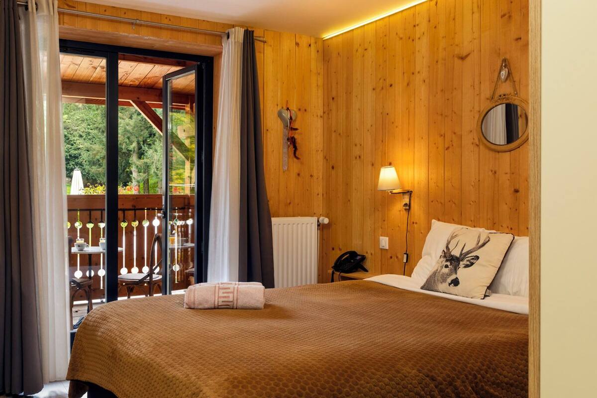 Een houten kamer met een bed, een nachtkastje, een lamp en uitzicht op een terras.