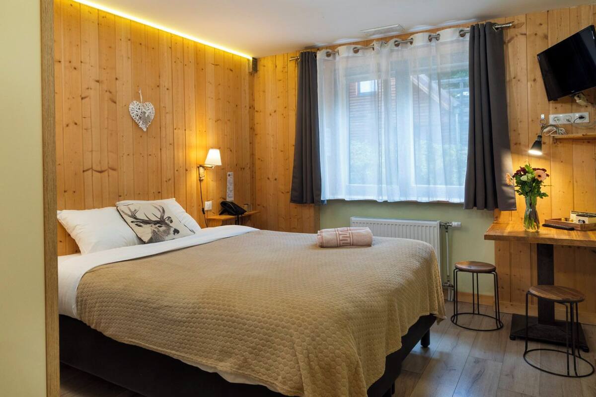 Een gezellige kamer met een bed, een bureau, een stoel, een televisie en een raam met gordijnen.