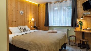 A cozy room with a bed, a desk, a chair, a TV, and a window with curtains.