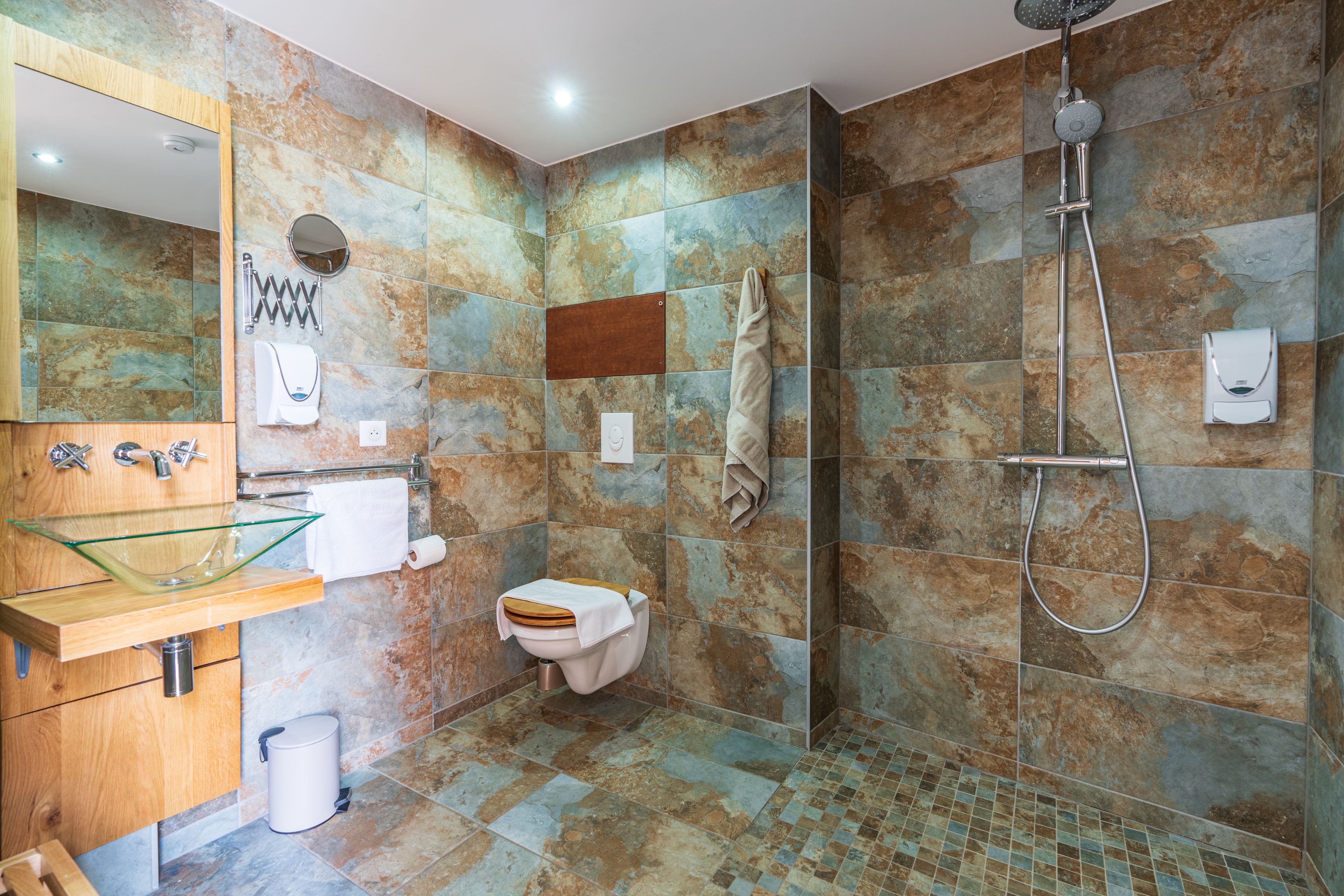 A modern bathroom with a glass sink, wooden vanity, a toilet, and a shower area.