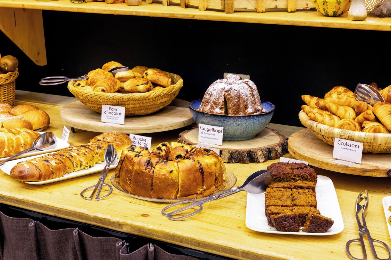 A bakery display with various types of bread and pastries, including pain chocolat, kougelhopf, brioche confichet, and croissant.