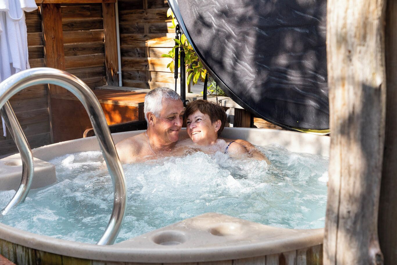 A couple in a hot tub with a wooden cabin background.