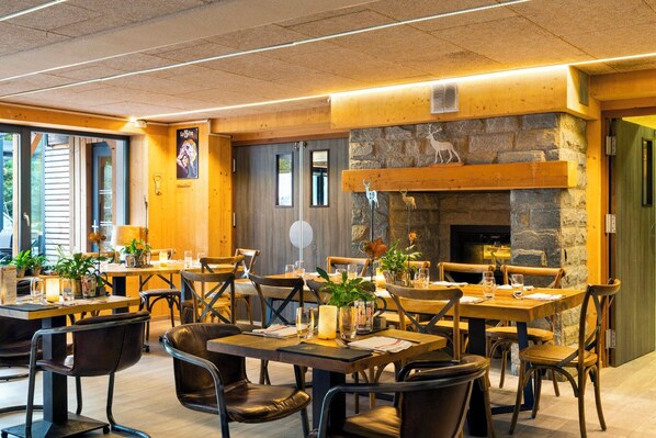 A restaurant with wooden tables and chairs, a stone fireplace, and a view through large windows.