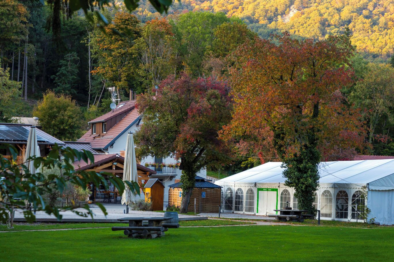 Un chalet rustique avec une façade en bois, un coin repas avec une table et des chaises, et une tente blanche en toile de fond.