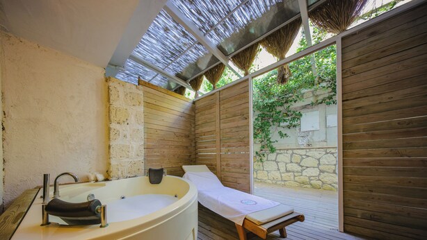 Un cuarto de spa con una tina grande, un banco de madera y una pared de piedra.