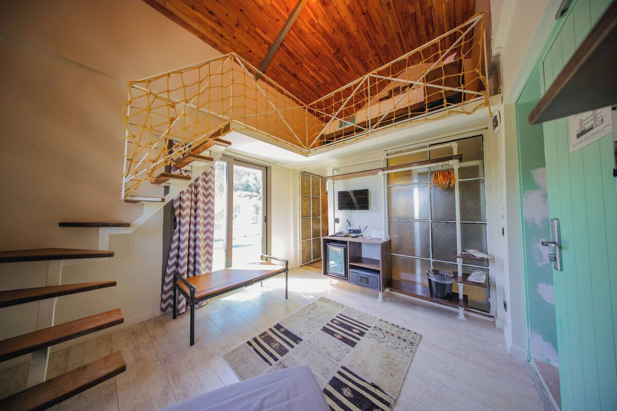 A spacious room with a wooden ceiling, a staircase with wooden steps, a bench, a television, a refrigerator, and a green cabinet.