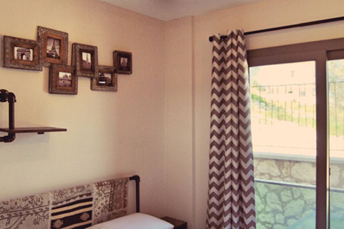 A bedroom with a bed, a wall-mounted shelf, and a window with a chevron-patterned curtain.