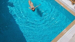 Piscina con una persona nadando, rodeada de sillas de descanso y plantas en macetas.