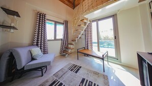 Amplia sala de estar con sofá, una mesita, una escalera y ventanas grandes.
