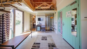 Una habitación amplia con techo de madera, un banco, un tapete estampado y vistas a una zona de cocina a través de una puerta de vidrio.