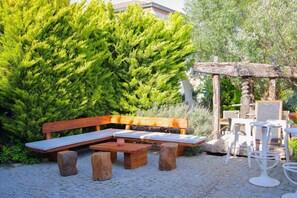 A wooden bench and table set in a garden with a large green bush in the background. - Brera Alacati (Cesme)
