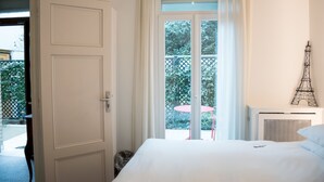 A hotel room with a large bed, a window with curtains, a view of greenery outside, and a small Eiffel Tower decoration on the wall. - La Villa Paris (Paris)