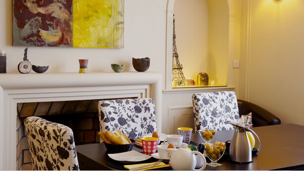 A dining area with a fireplace, floral-patterned chairs, a table set with a basket of bread, cups, and a teapot. - La Villa Paris (Paris)