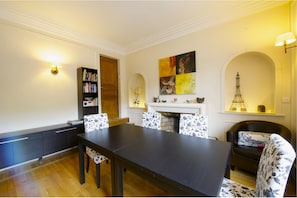 Un comedor con una mesa y sillas de madera oscura, una estantería, una chimenea y un cuadro decorativo.